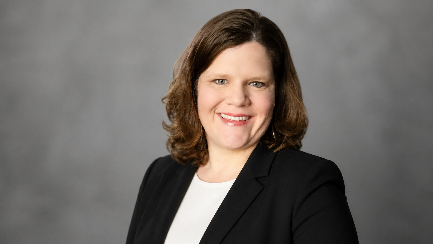 Susie Likovic, founder of Uplevel Assistance, smiling in a black blazer against a gray backdrop