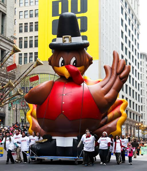 A giant inflatable turkey balloon float in the Chicago Thanksgiving Parade, guided down the street by volunteers in white shirts